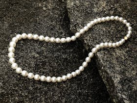 A strand of lustrous Kailis Australian South pearls sits delicately on a rock