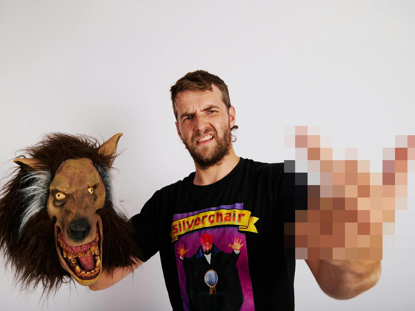 Auto-tune performer holds a wolf mask in one hand and makes a gesture with the other.
