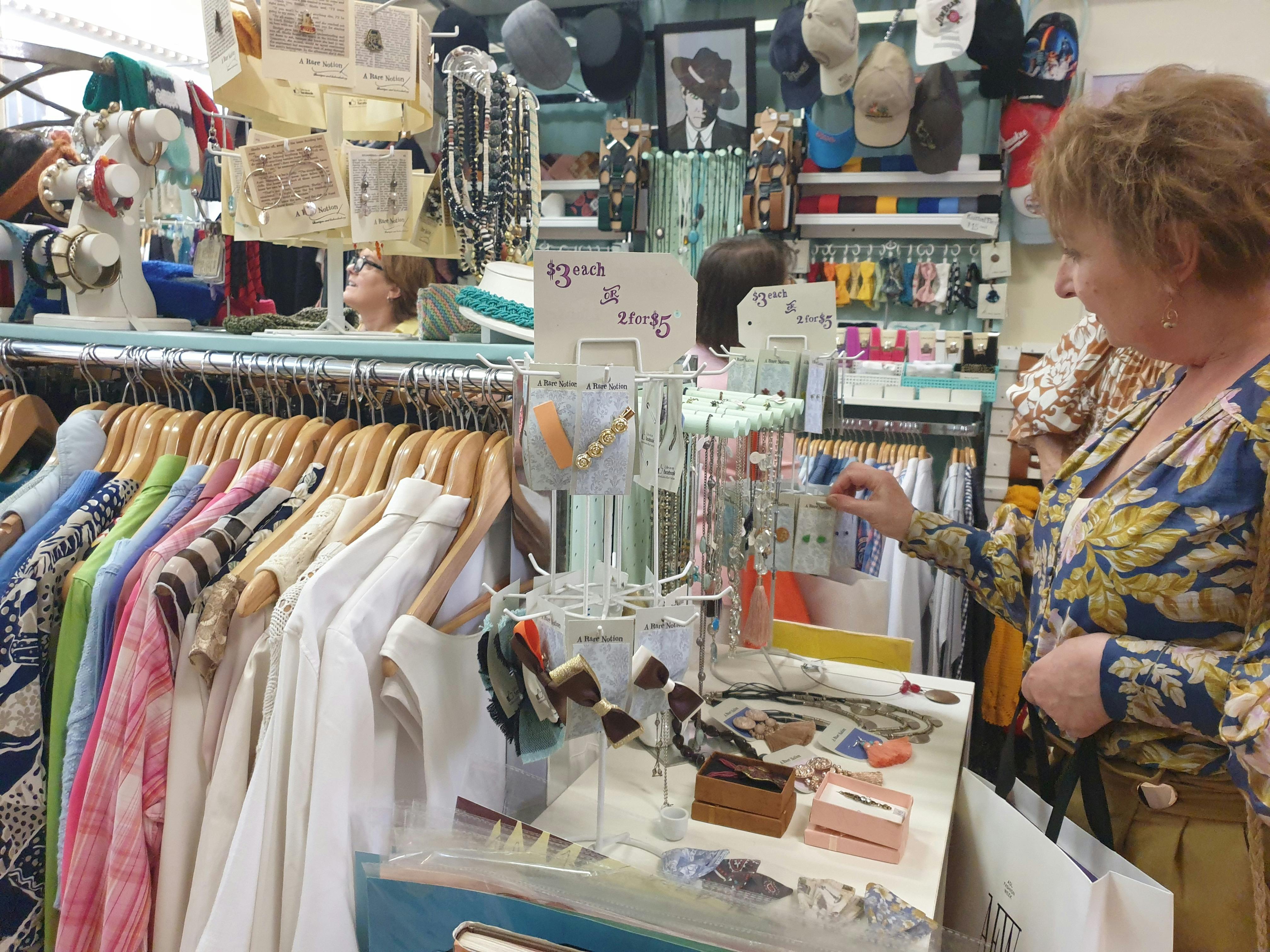 A woman looks at accessories on a small rack in a preloved clothing store.