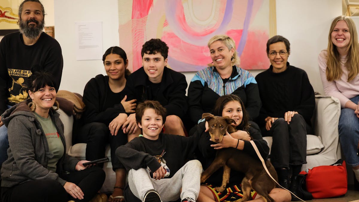 a beautiful aboriginal family sit on the coach at Munimba-ja smiling and holding kelpie pup