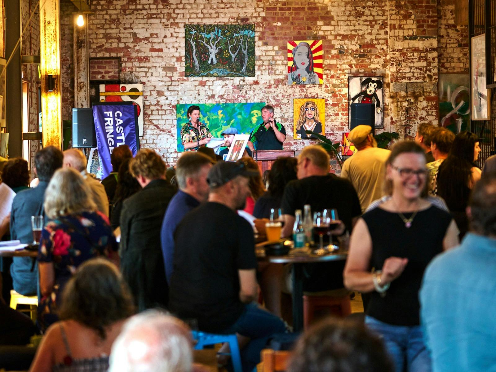 A photo of a crowd of people in a pub with artwork onstage being auctioned off