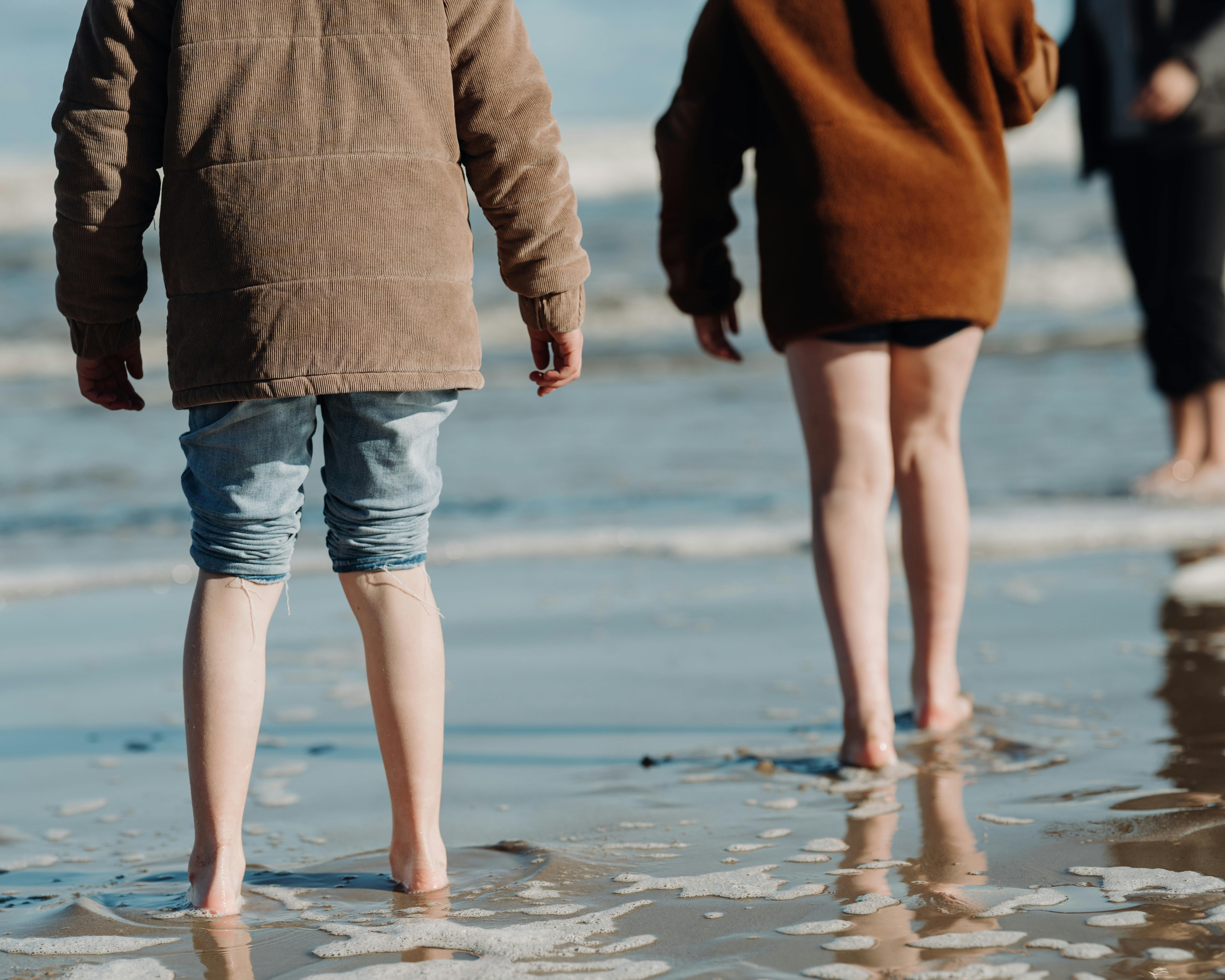 Three people stand barefoot on the wet sand at the beach,  looking for Goolwa pipis