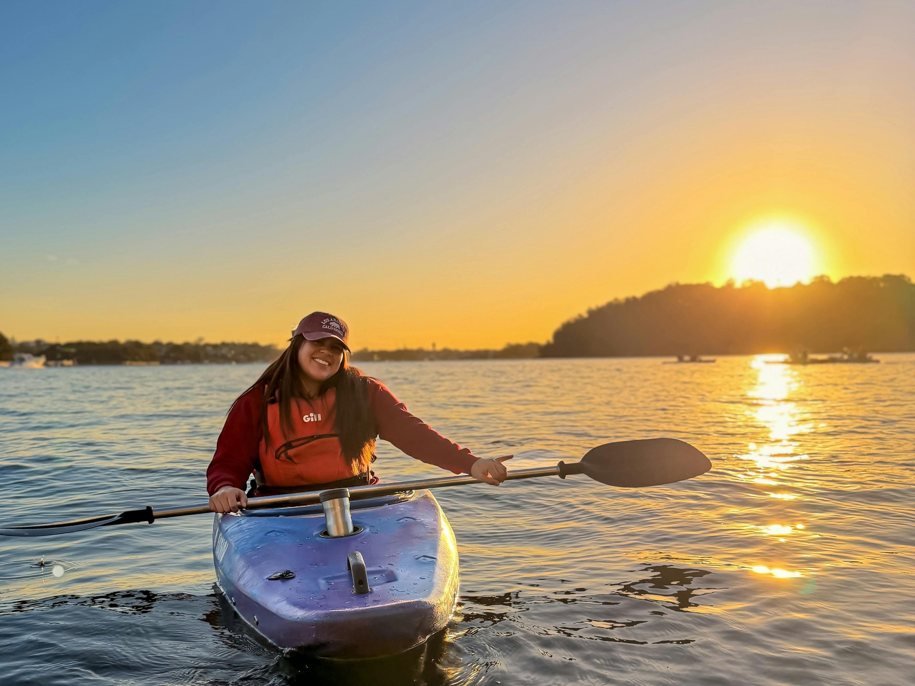 The sun sets behind goat island while a girl gets free photos from her Sydney By Kayak guide.