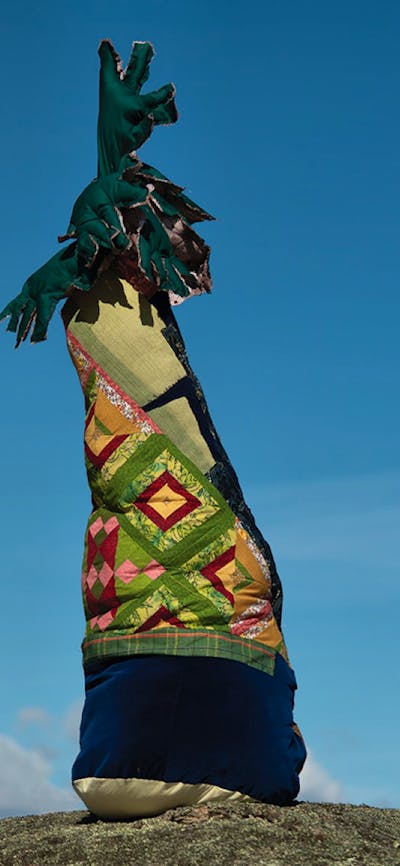 A textile tree sitting on top of a hill. The trunk is with quilts with plush leaves on the top.