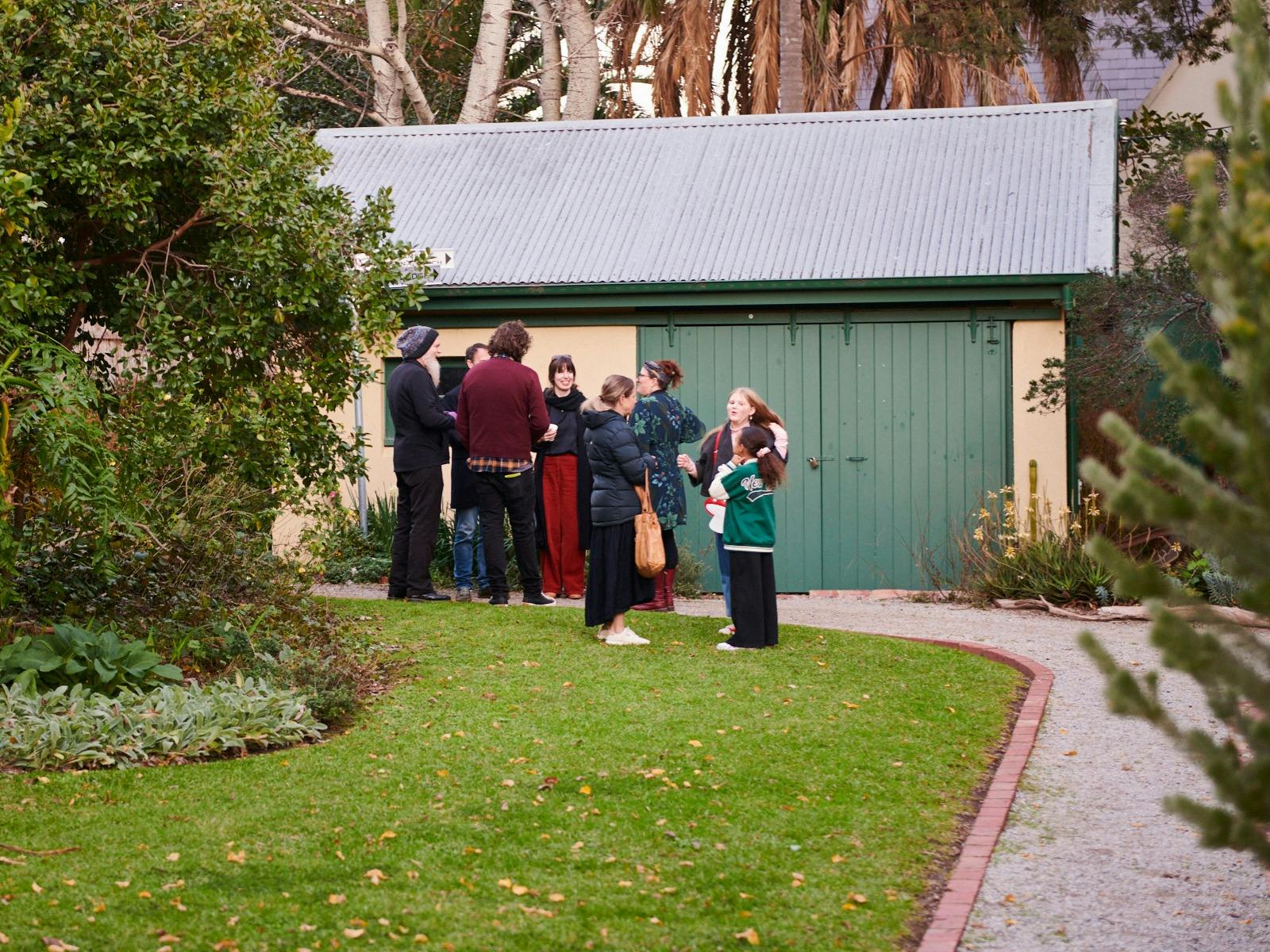 A small group of people gathered outside a green shed in a Heritage Hill and Historic Gardens.