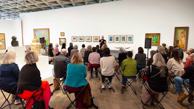 Photo of a group of people sitting in a gallery listening to someone talk