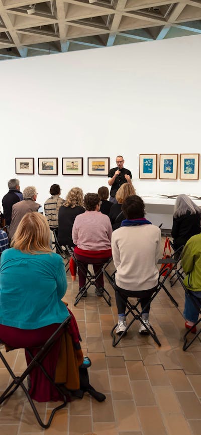 Photo of a group of people sitting in a gallery listening to someone talk