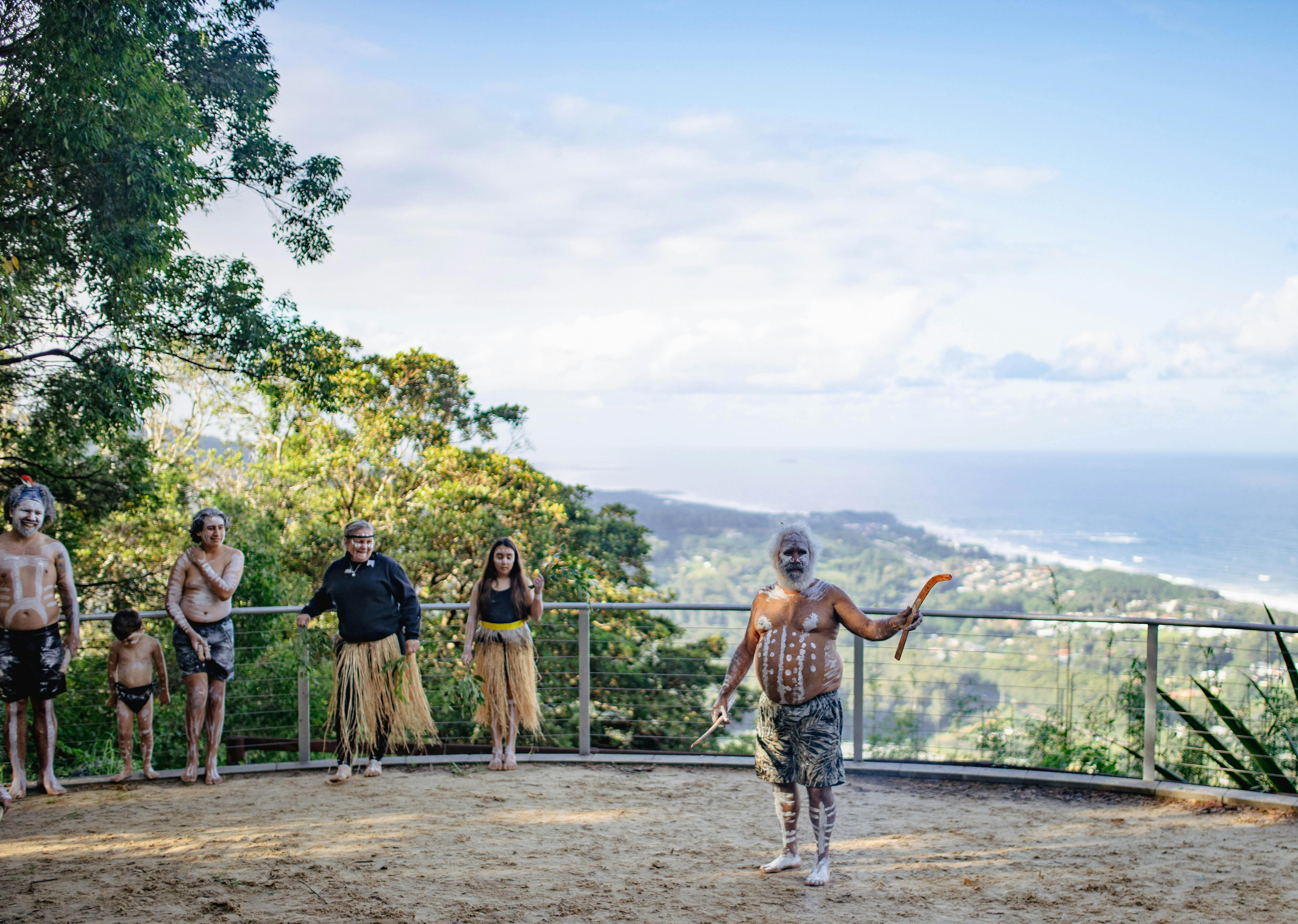 Aboriginal man standing in front of scenic views, introducing cultural dance performance.