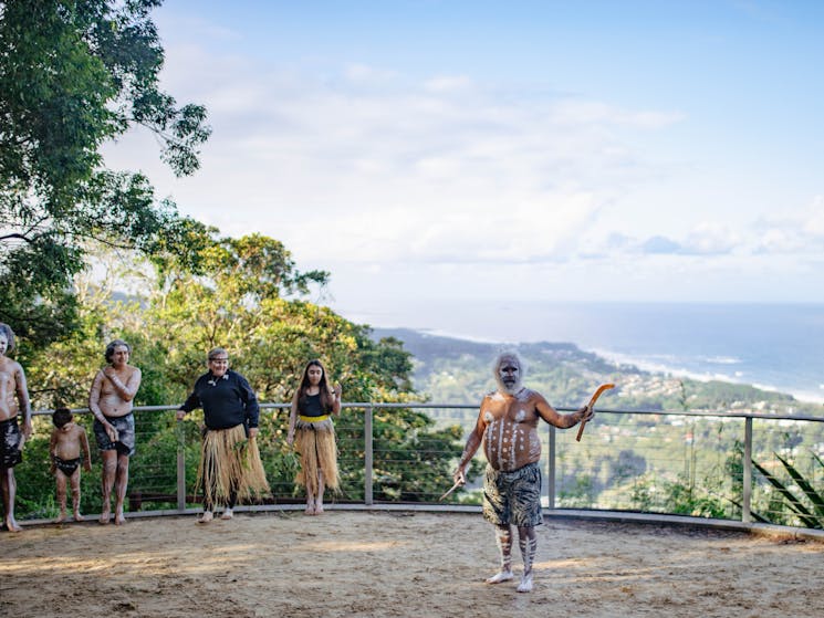 Aboriginal man standing in front of scenic views, introducing cultural dance performance.