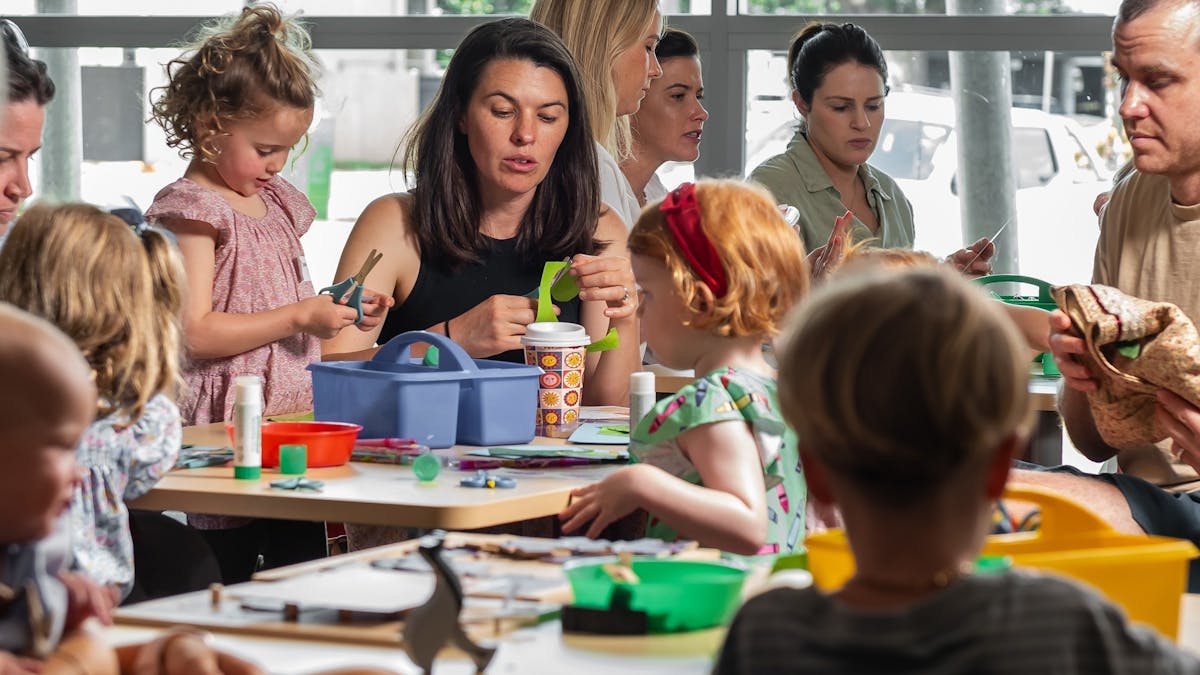 Parents and children sit at tables together and use crafts.