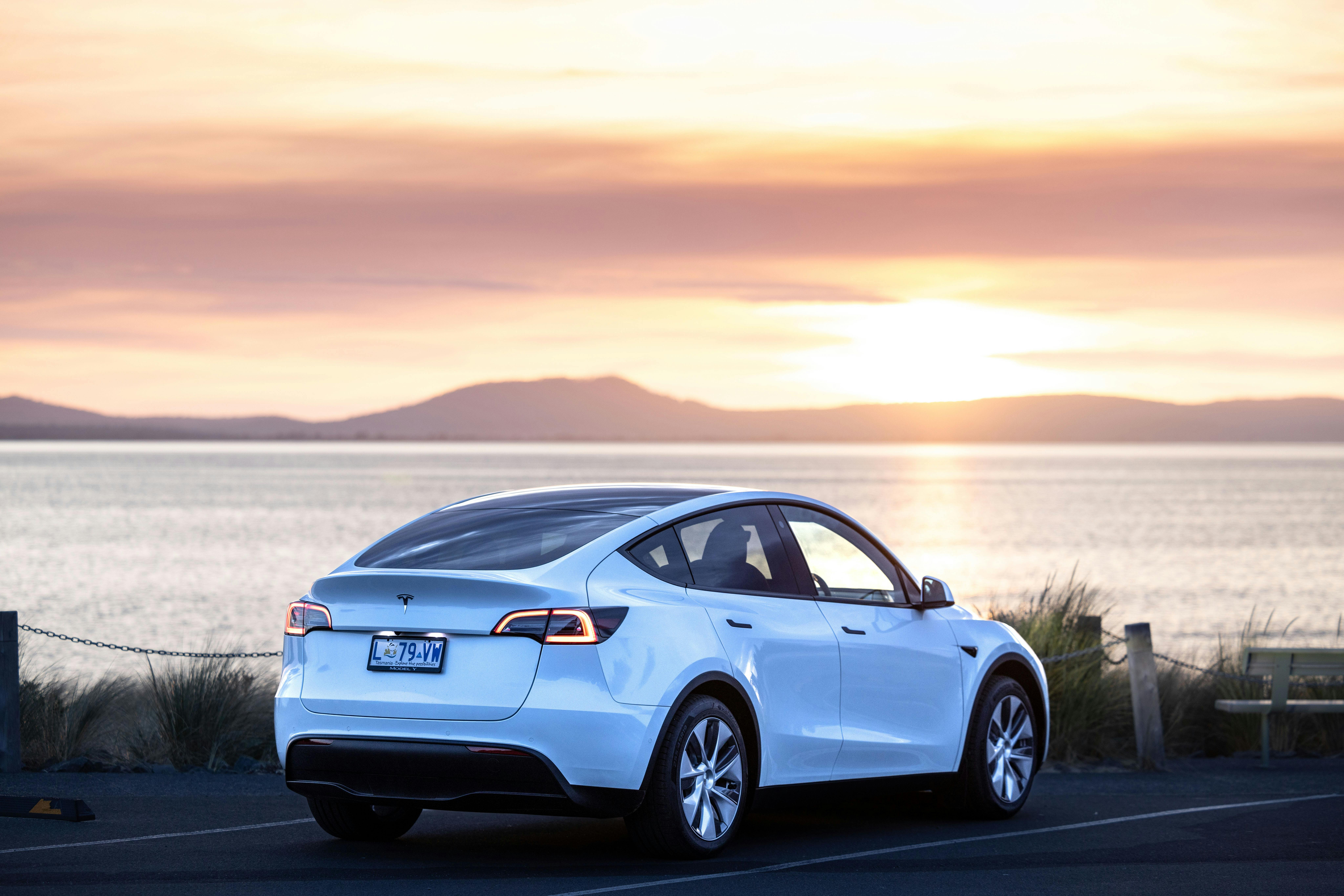 Electric vehicle hire car (Tesla Model Y) parked at the beach at sunrise in Swansea, Tasmania..