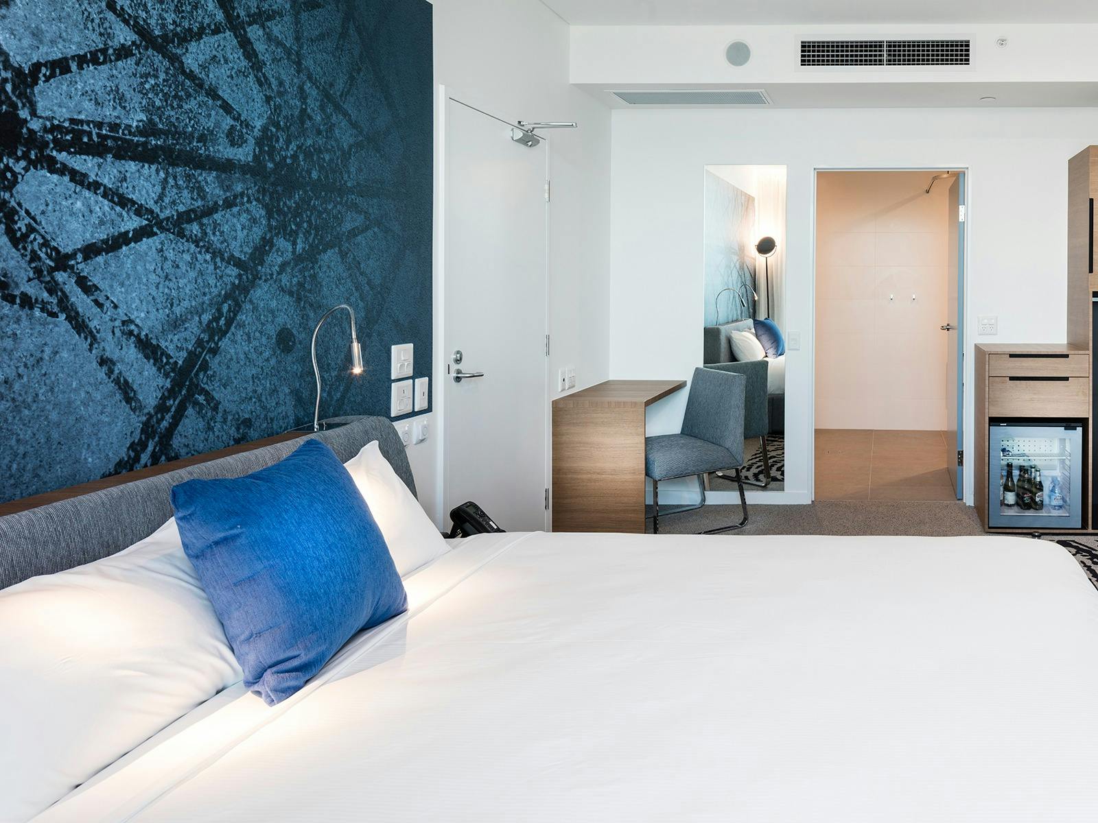 Room with bed in white sheets, blue cushion and blue panels in the wall Room with bed in white sheets, blue cushion and blue panels in the wall