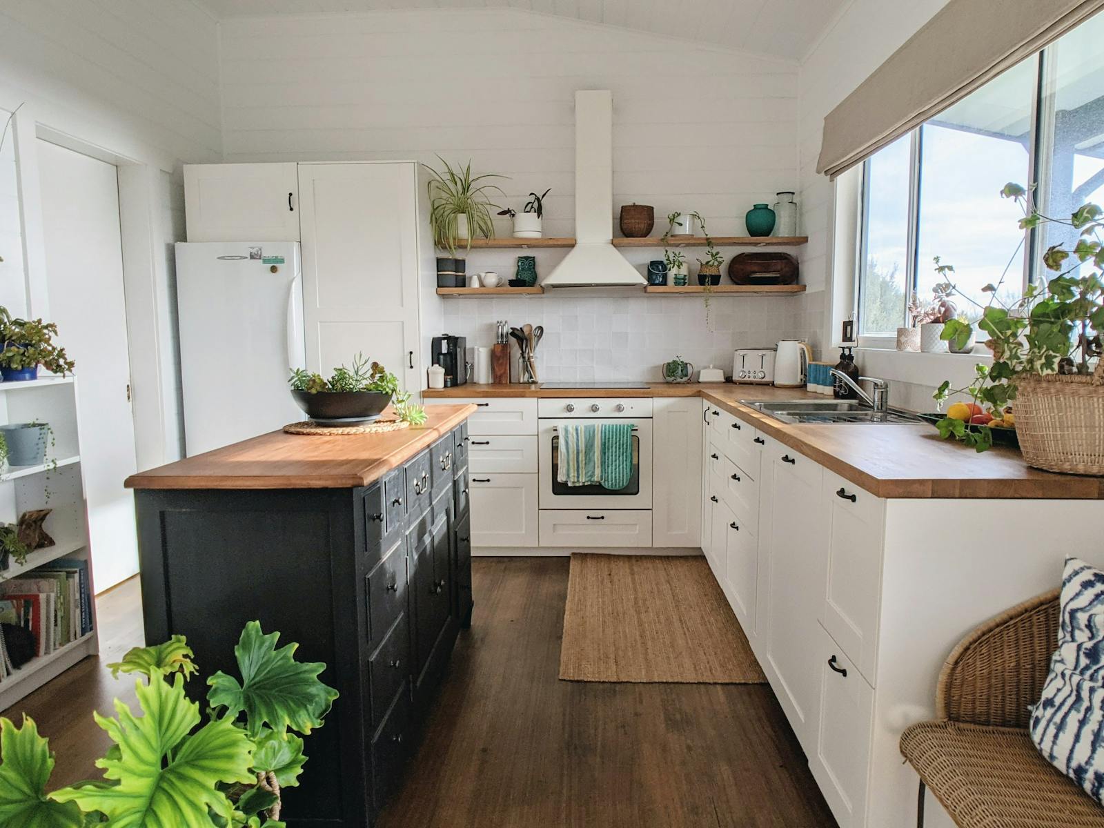 Kitchen with white cabinets and timber benchtop. A black coloured island bench with plant