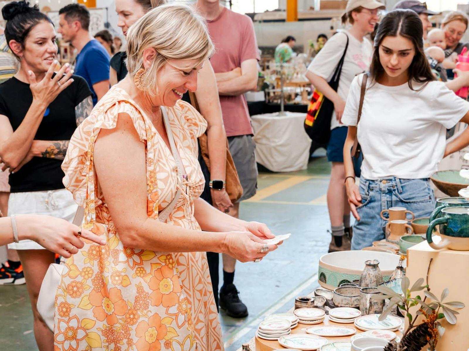 A women standing at a stall holding a piece and looking at it smiling