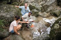 Aboriginal guide at Mossman Gorge with guests, demonstrating ochre paints by the creek.