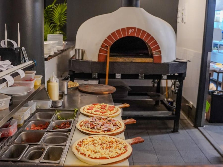 three pizzas lines up in front of a traditional pizza oven