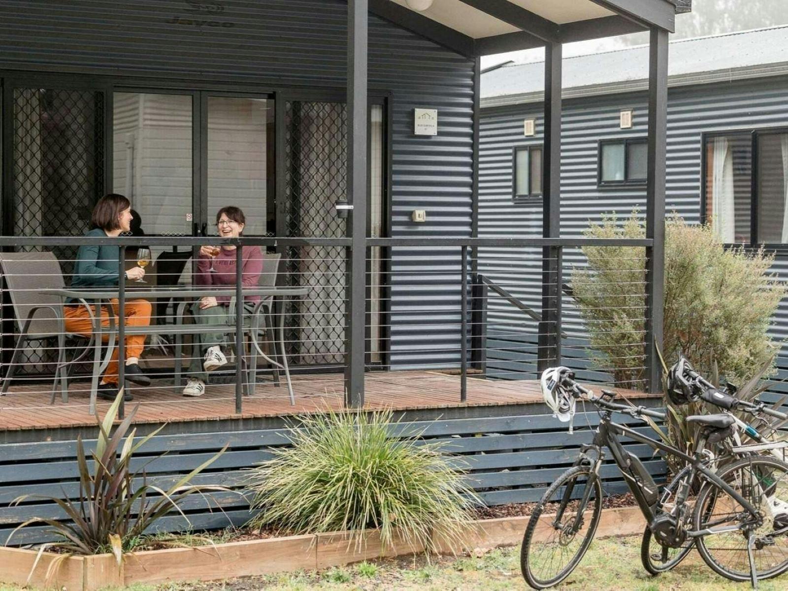 Guests relax on their deck with wine, overlooking Victoria’s High Country after cycling the Rail Tra