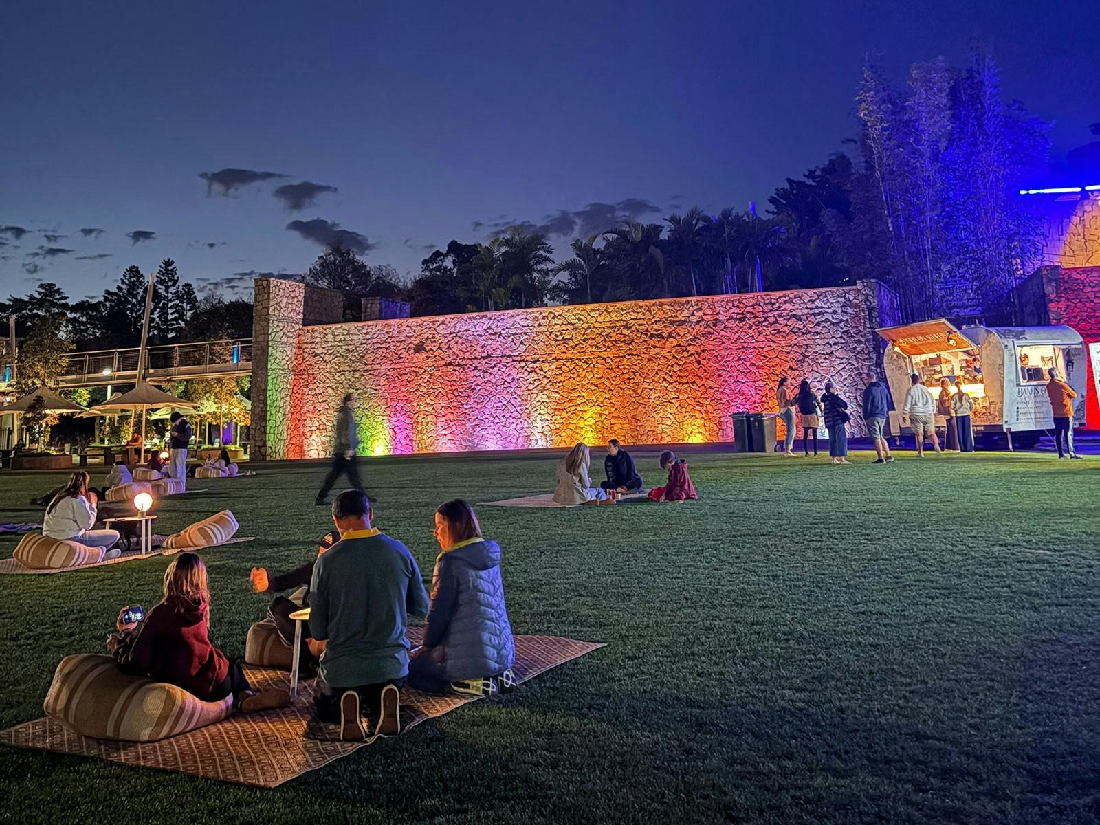 Lawn area outside at night people sat on picnic rugs and coloured backdrop lighting