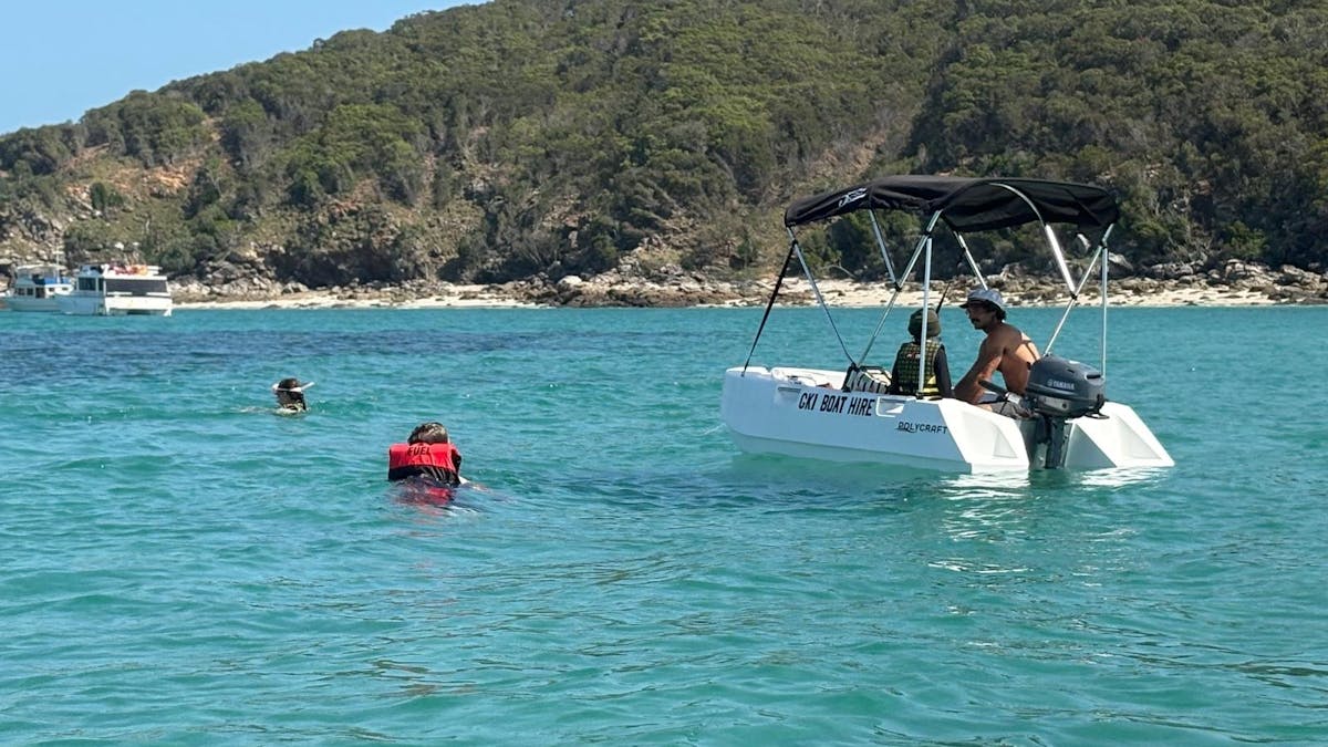 Two swimmers near a white Polycraft hire boat in calm water at GKI.