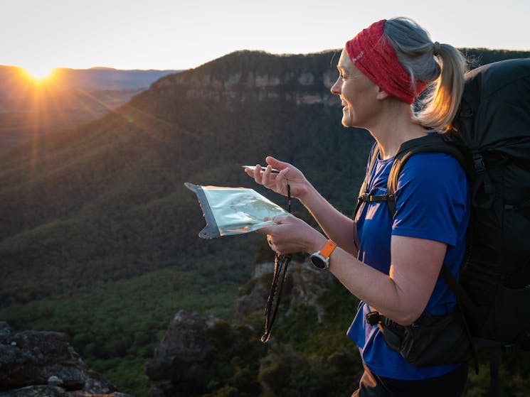 Woman stands on cliff in bush with map and compass looking to horizon