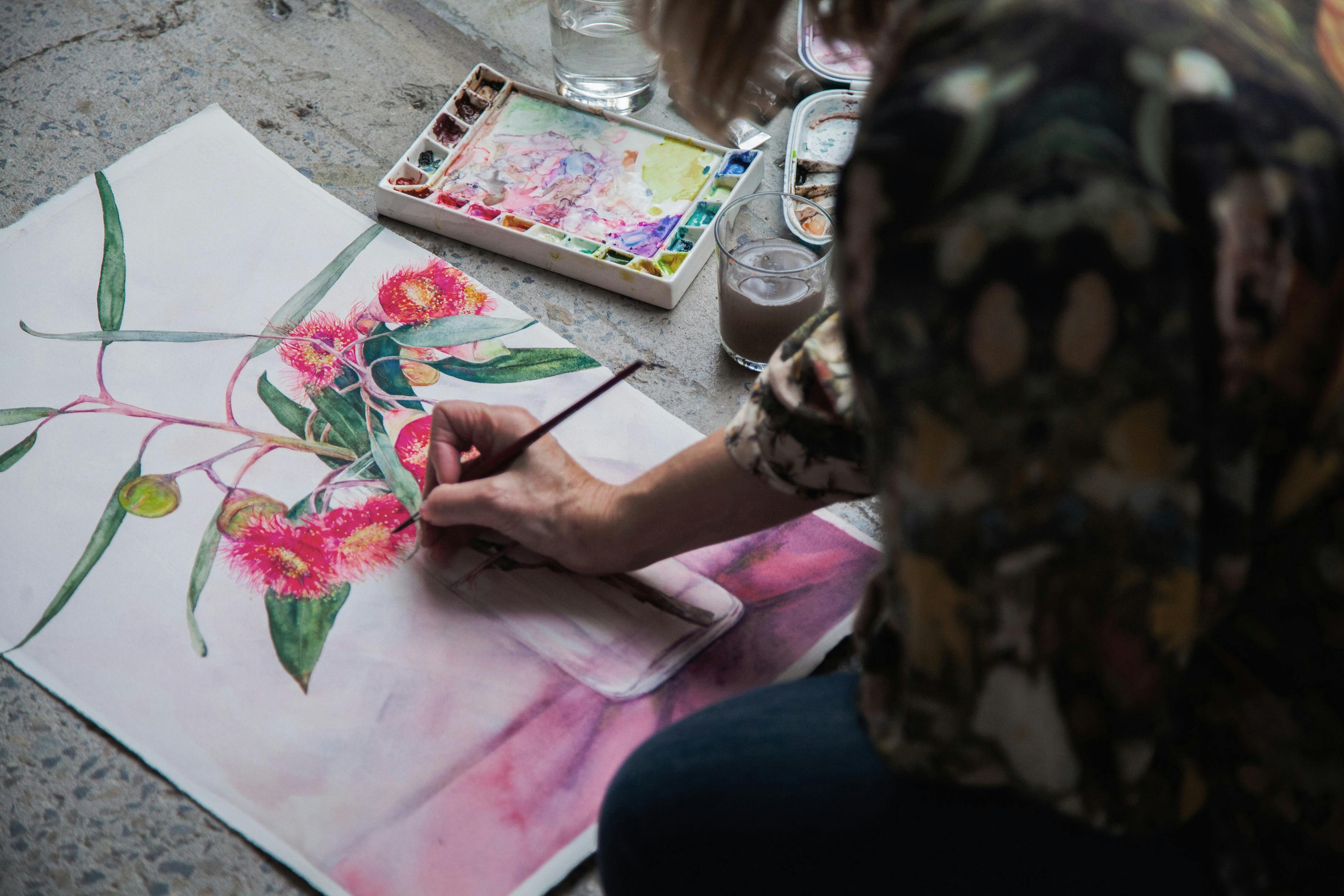 Artist painting pink flowering gum blossoms in watercolour, palette and brush in hand.