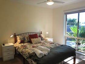 Bedroom with queen sized bed, bedside tables with lamps and large window beside bed. Ceiling fan