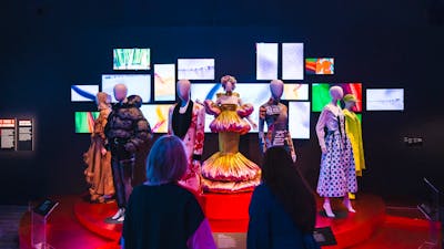 A dimly lit exhibit showcases mannequins dressed in Korean fashion on a red circular platform.