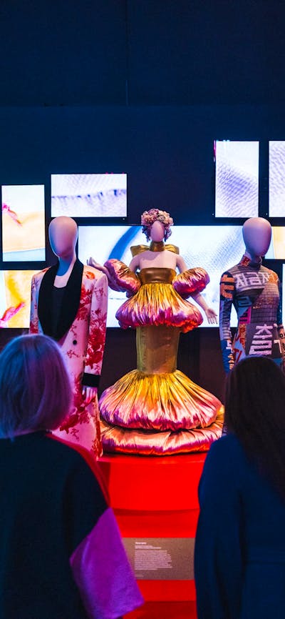 A dimly lit exhibit showcases mannequins dressed in Korean fashion on a red circular platform.