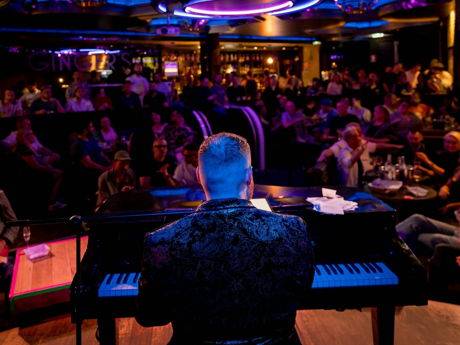 A pianist at a keyboard facing an audience in a colourful live music bar.