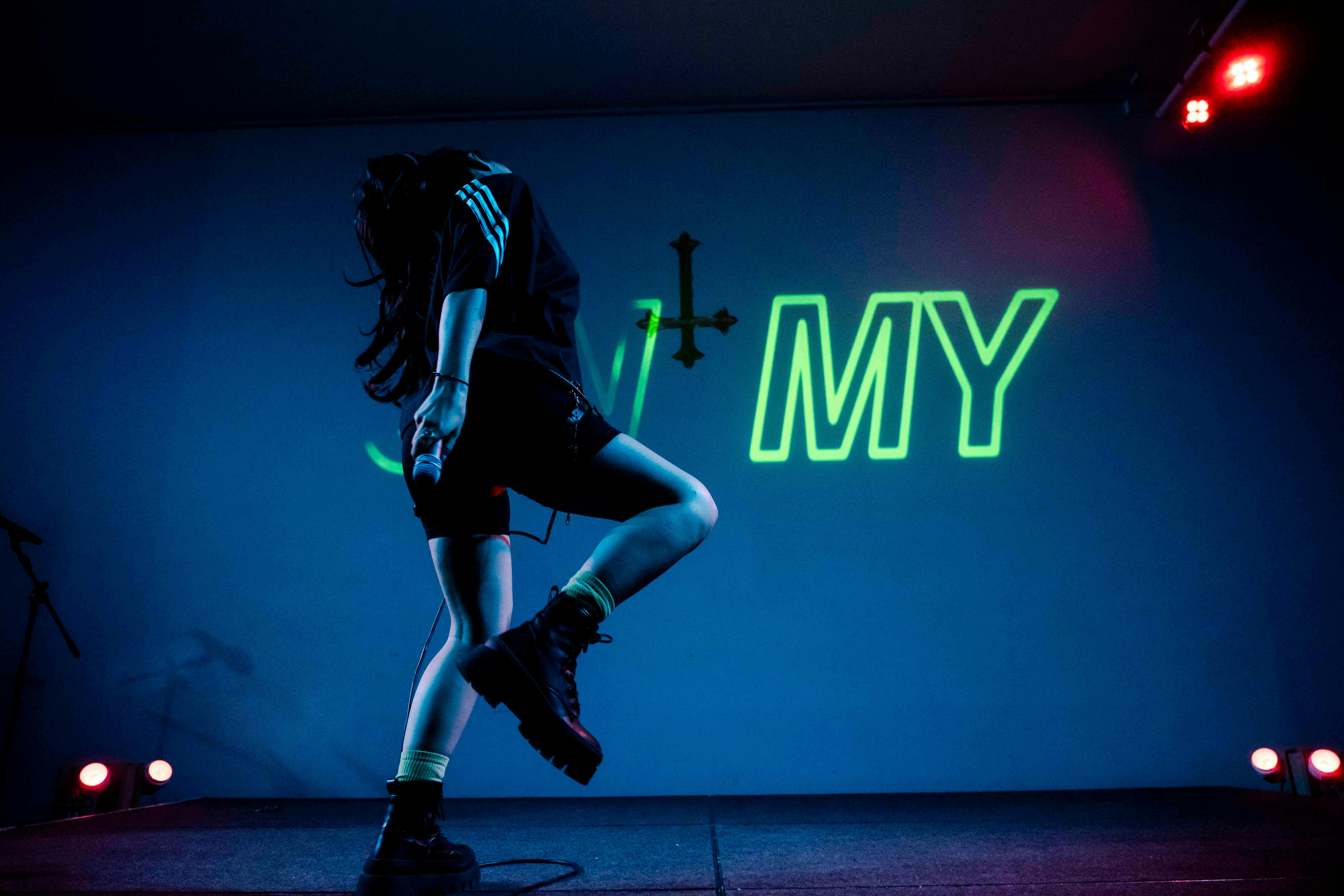 Singer is dancing with her head turned down against a blue backdrop