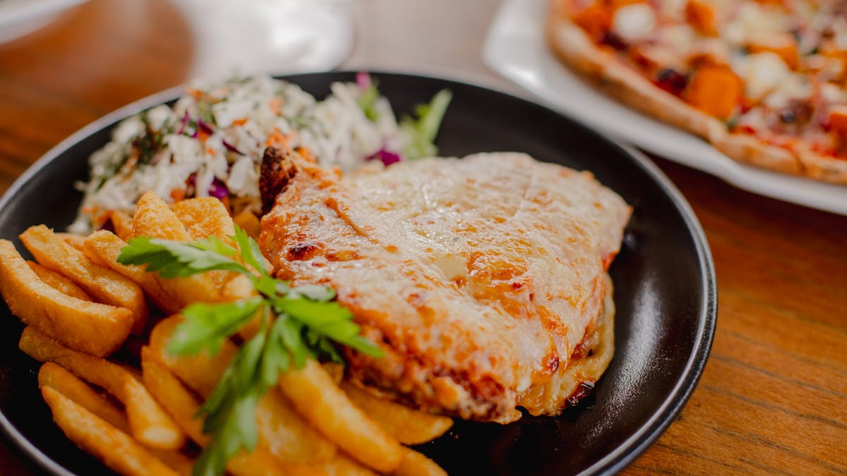 Plate of chicken parmigiana, chips and salad on a table at Orion Hotel Springfield