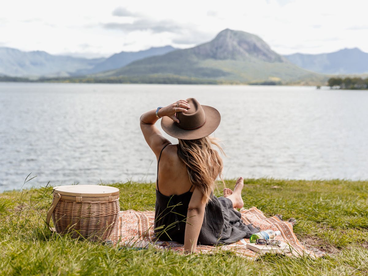 A woman sits on a picnic rug looking across a lake to the distant mountain