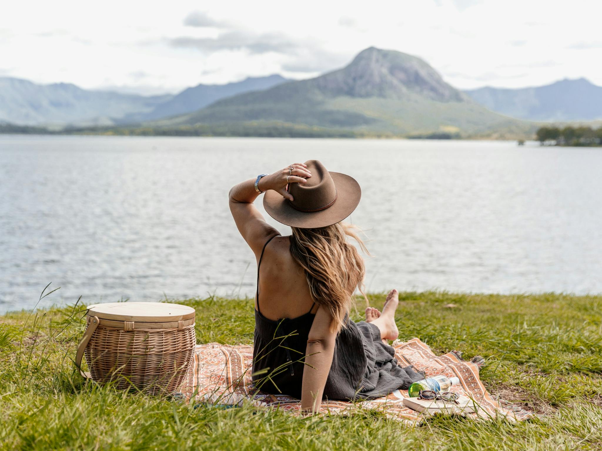 A woman sits on a picnic rug looking across a lake to the distant mountain A woman sits on a picnic rug looking across a lake to the distant mountain