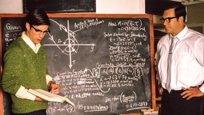 Two men stand with a blackboard with calculations on it