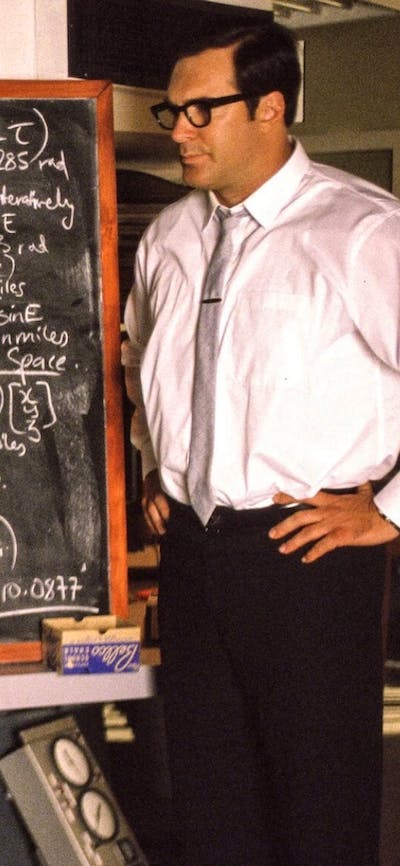 Two men stand with a blackboard with calculations on it