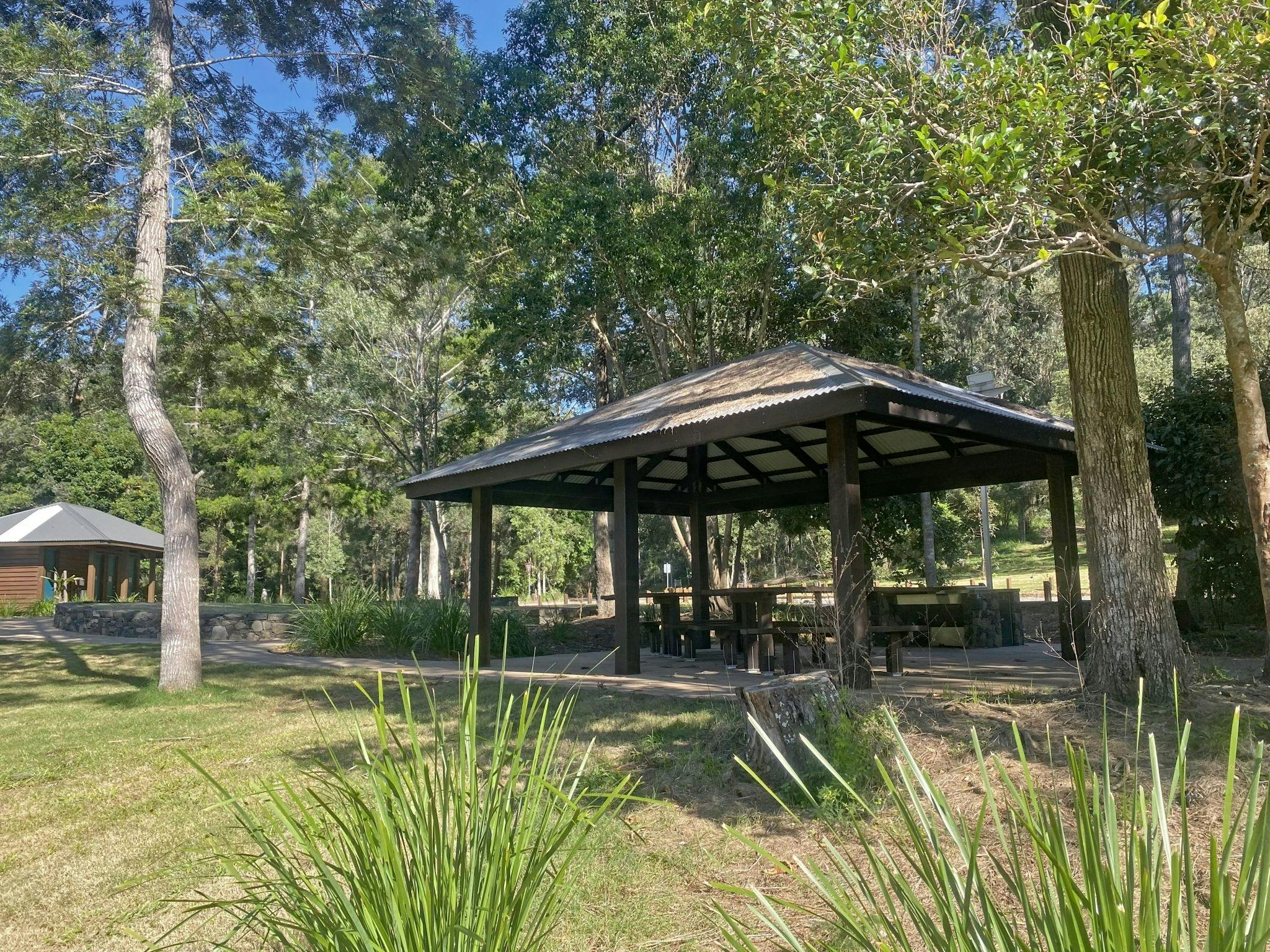 Sheltered picnic tables in grassy area with a toilet block in the background. Sheltered picnic tables in grassy area with a toilet block in the background.