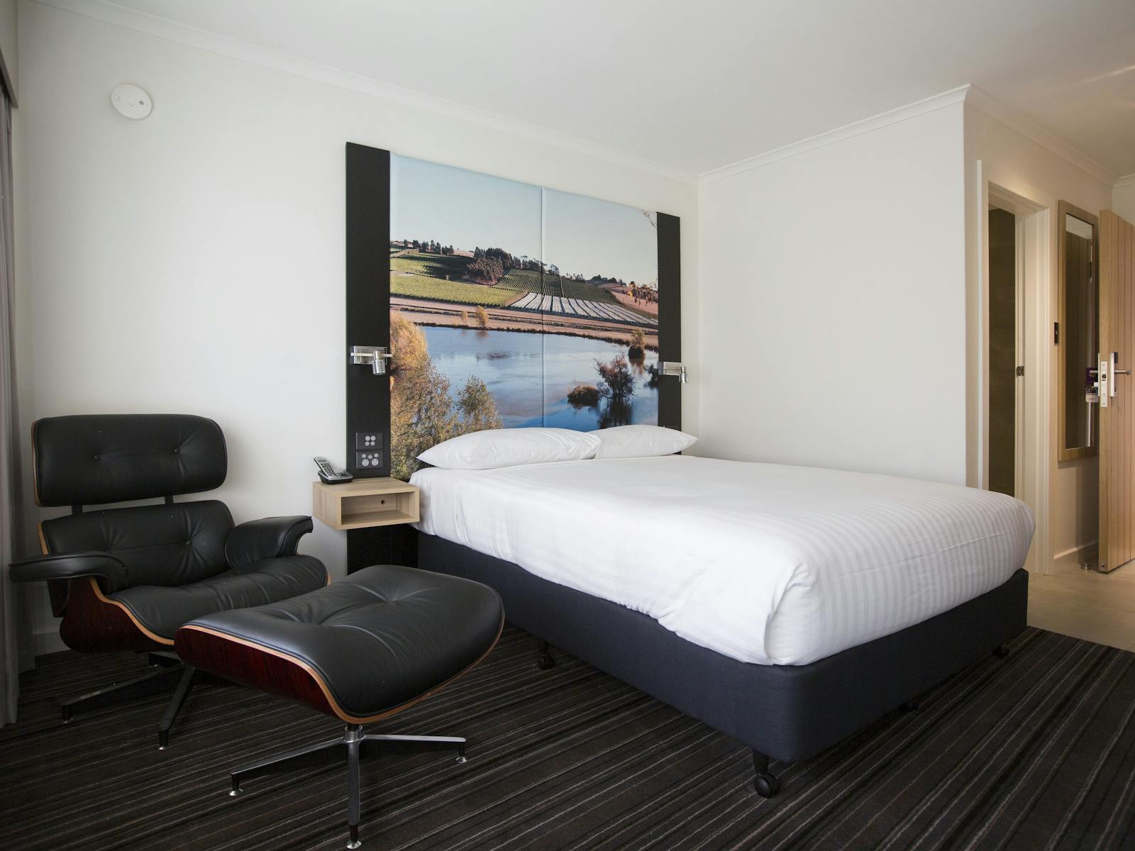 Guest accommodation room, with queen bed and sitting chair with footstool, large picture bedhead.