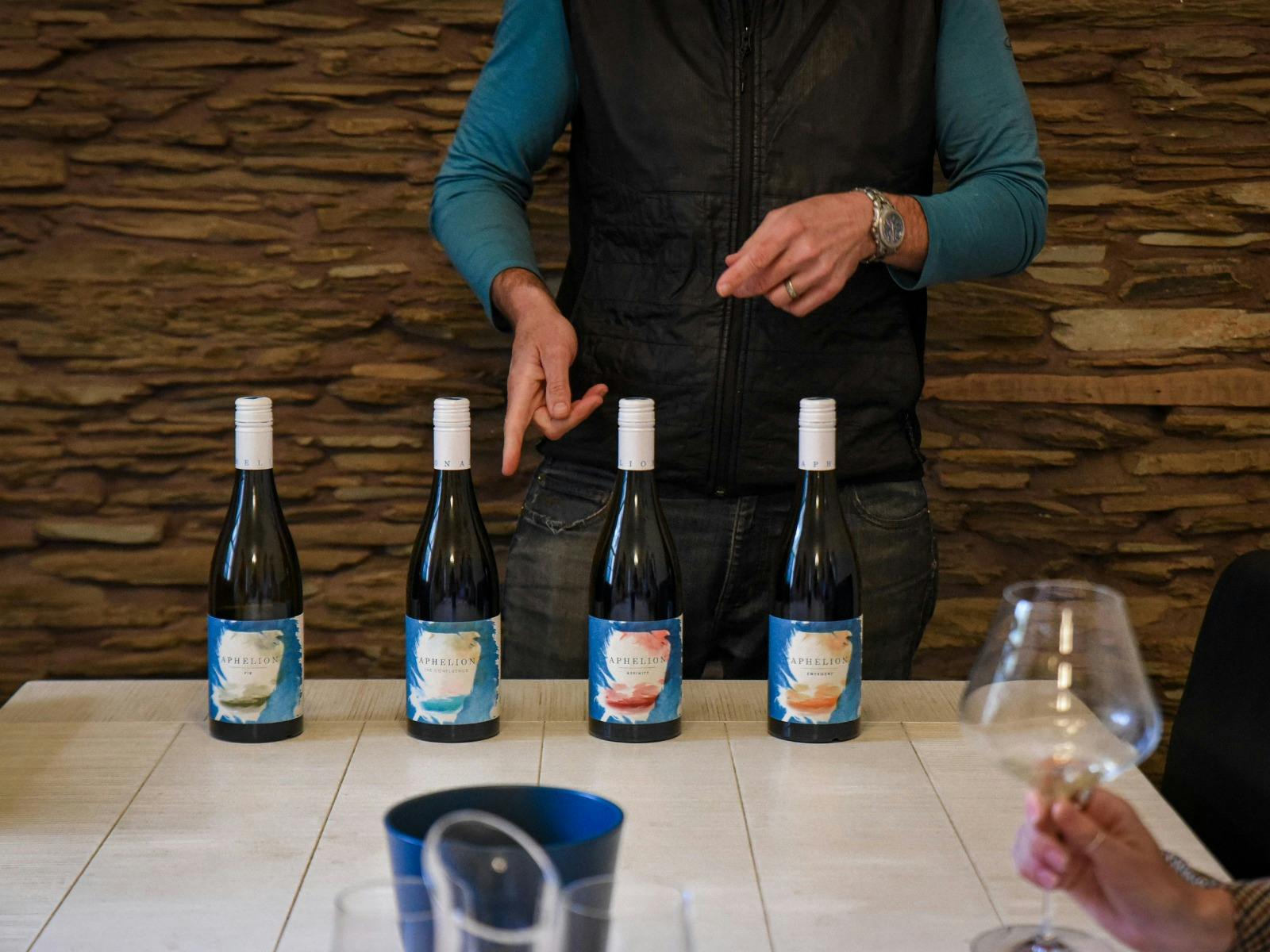A man pointing at a row of wine bottles on a white table