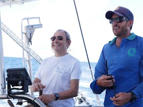 Guest taking the helm under watchful eye of the skipper Ocean Free sailing, GBR , tropical island