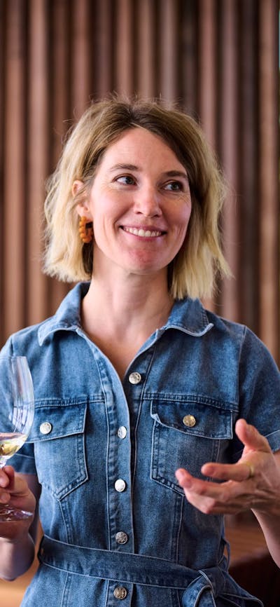 A woman holds a glass of wine and is gesturing with her other hand