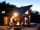 Four guests sit around a glowing fire pit in front of a timber log cabin at dusk in the High Country