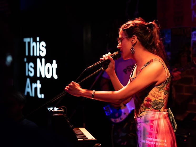 Person singing into a microphone with a This is Not Art sign in the background
