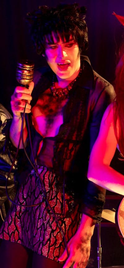 Two people playing on stage in a dimly lit setting, woman wearing cat ears