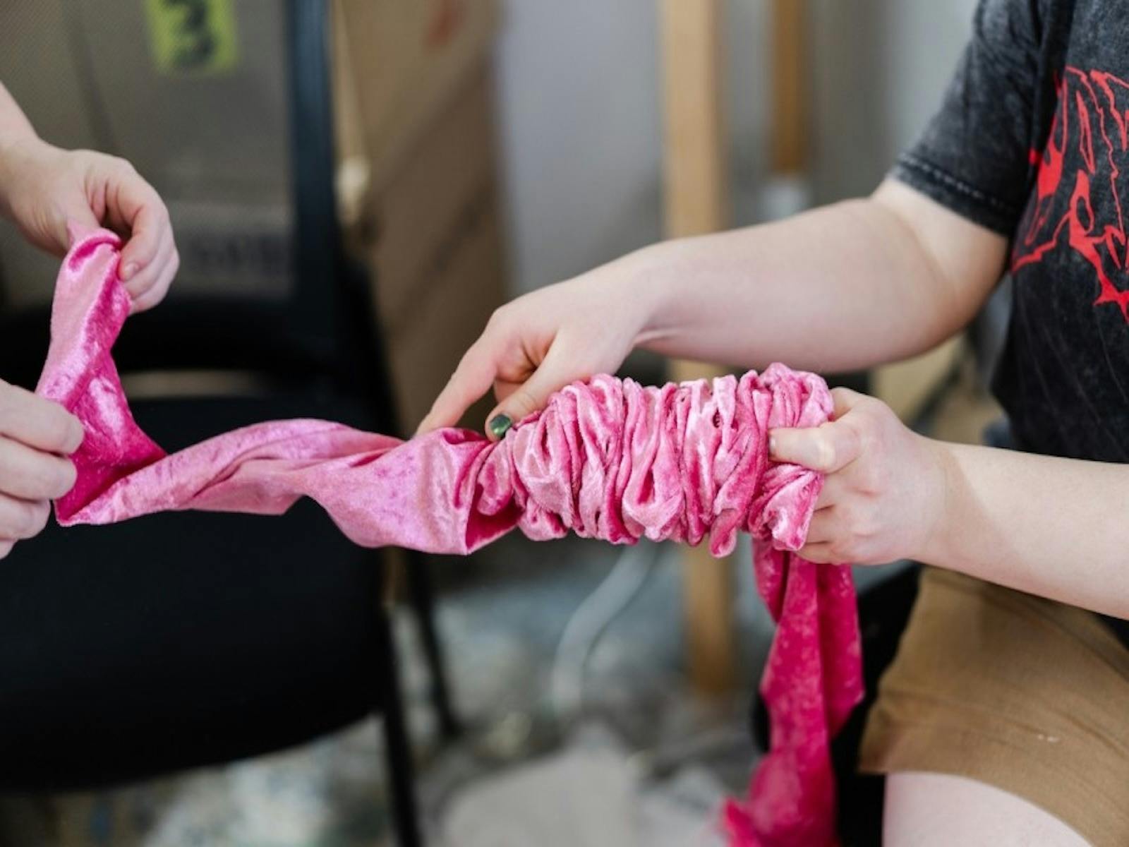 Two people manipulating a piece of bright pink, ruched fabric. One person tightly gathers the materi