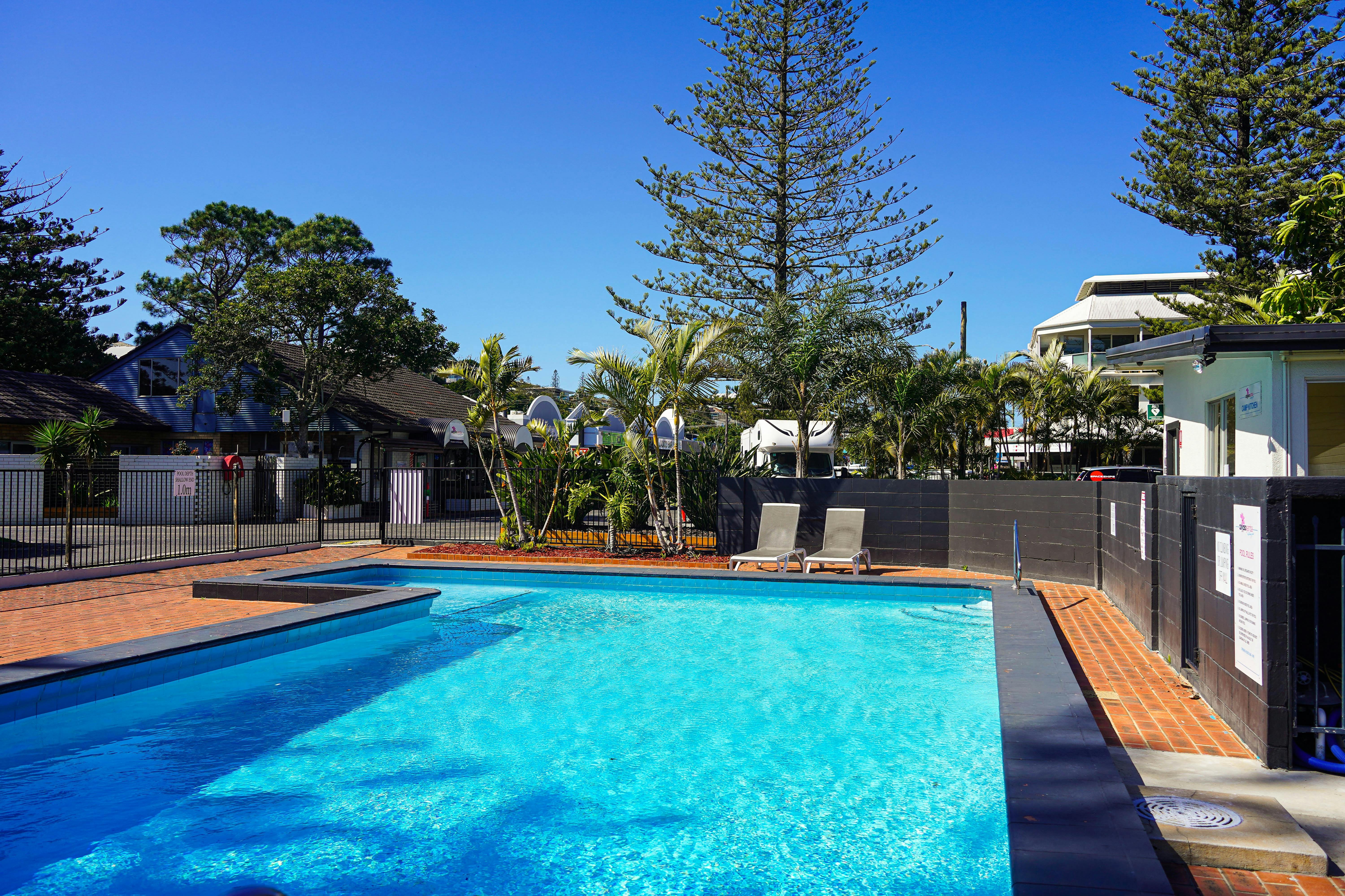 在陽光明媚的日子裡，一個寬敞的藍色游泳池裡擺放著兩張日光躺椅。