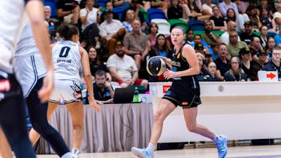UC Capitals player dribbling a basketball while being defended.