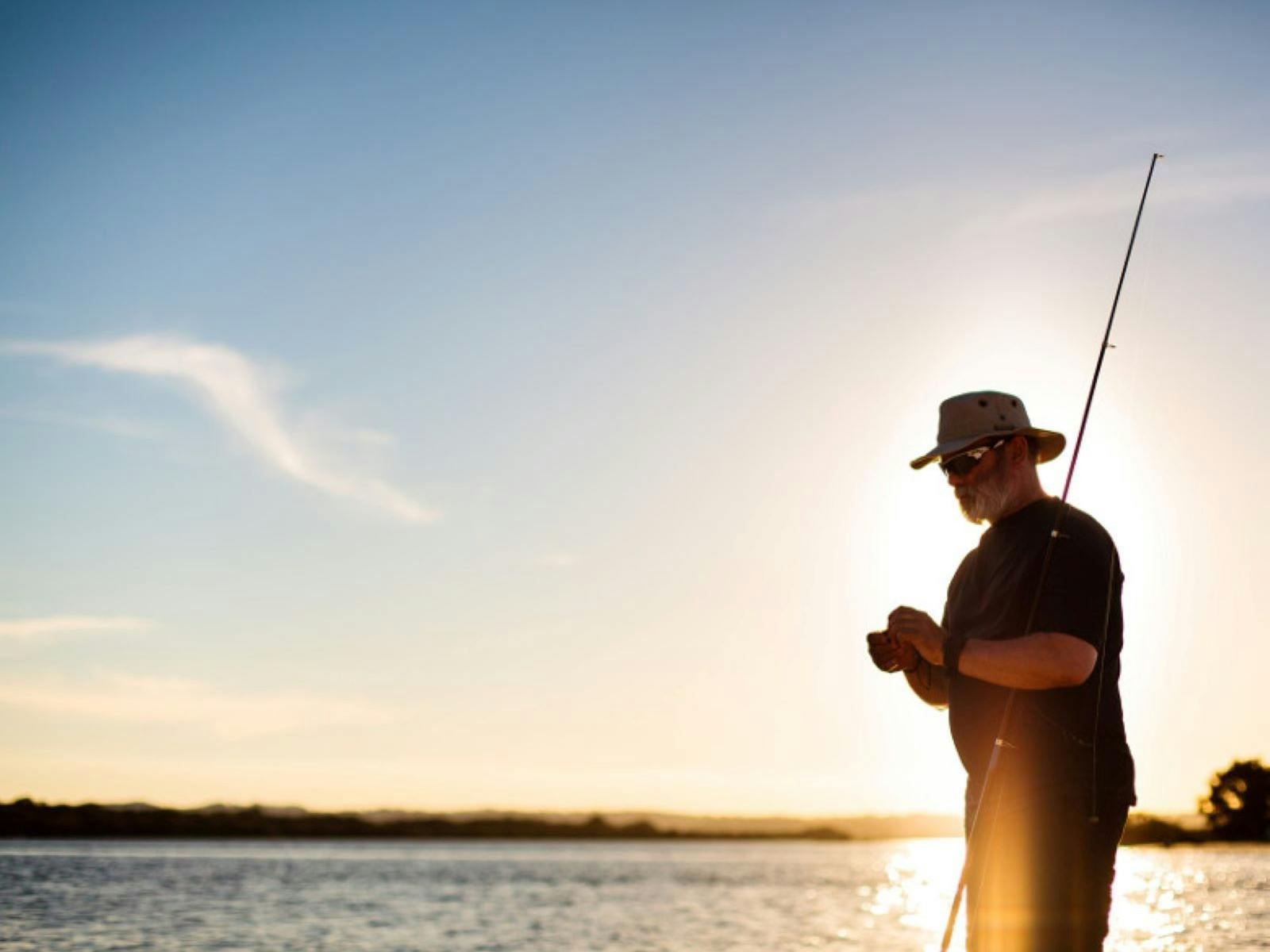 Man baiting a hook with sunset in background
