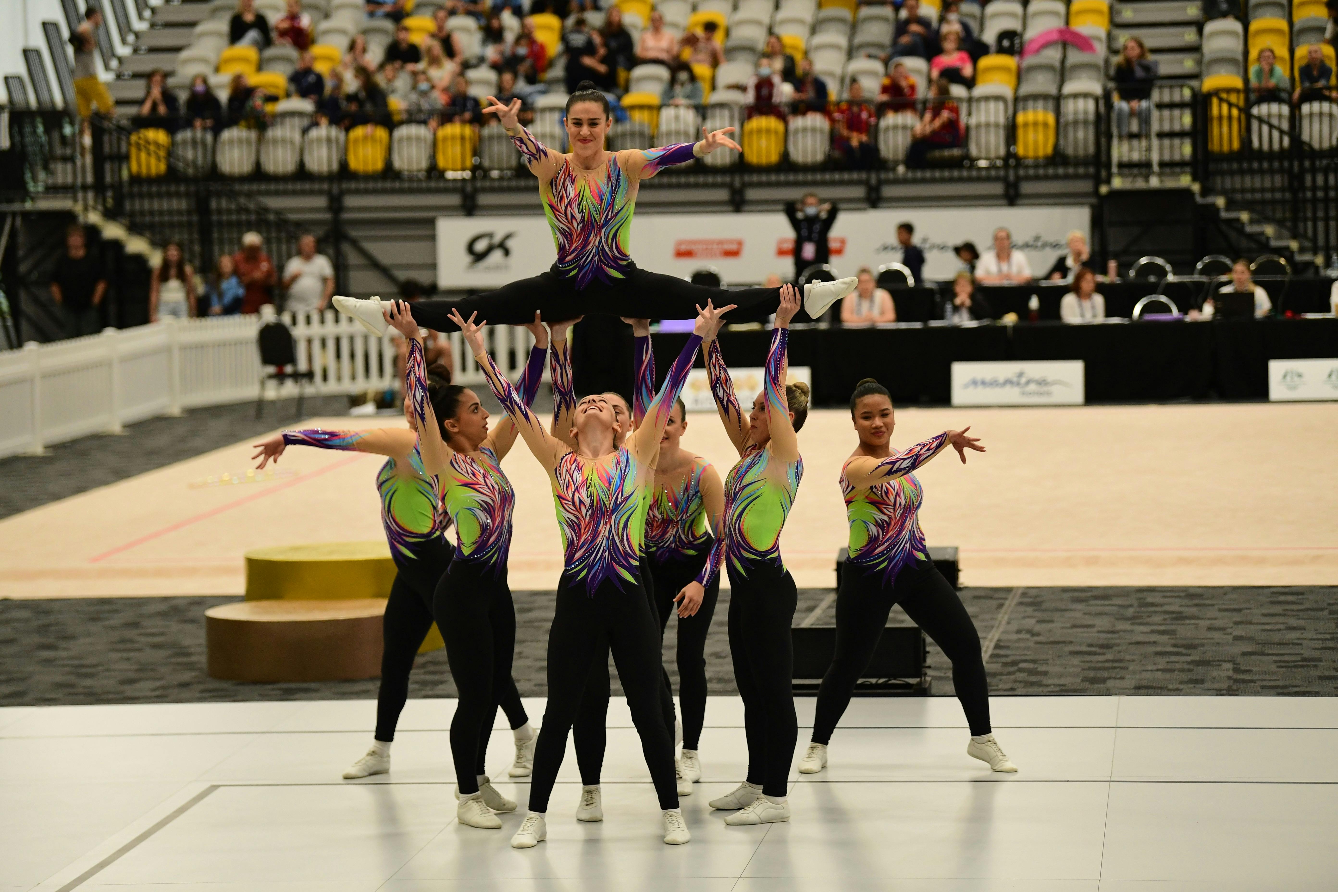 Group of gymnasts pose with athlete being held in the air