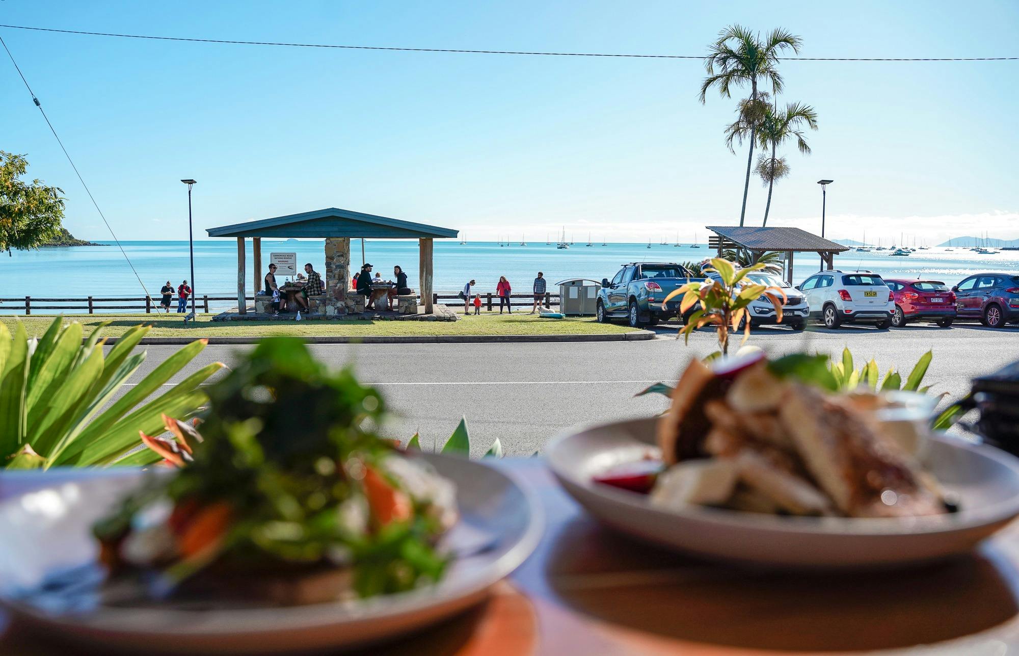 View from a cafe window with food on the table overlooking the ocean and picnic area