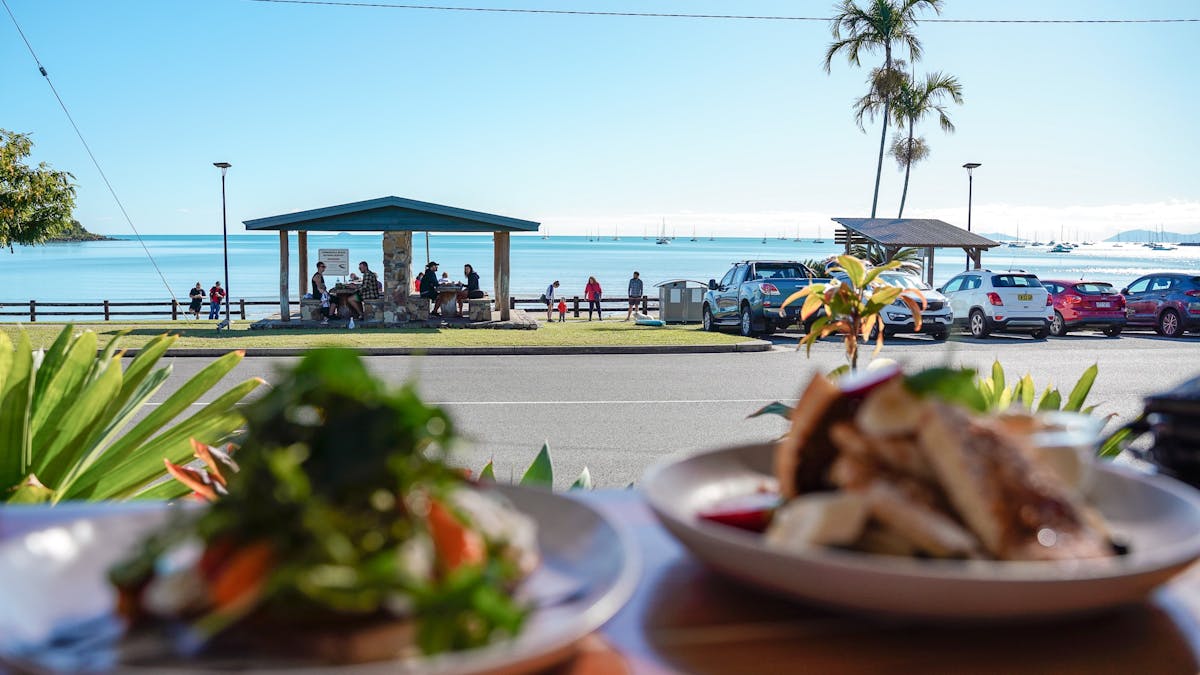 View from a cafe window with food on the table overlooking the ocean and picnic area